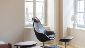 A modern room with a black chair, a small round table, and a view of buildings through a large window. - Elegant Family Apartment in Como centre (Como)