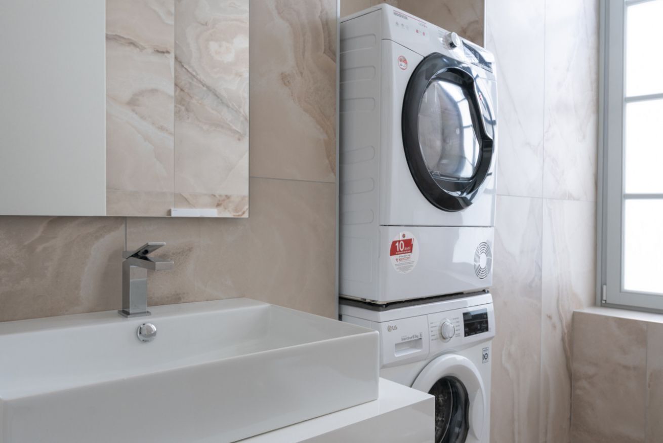 A modern bathroom with a built-in washing machine, a sink, and a marble backsplash.