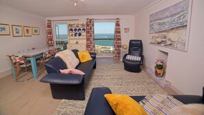 Ein Wohnzimmer mit einer Couch, einem Sessel, einem Esstisch und Meerblick.