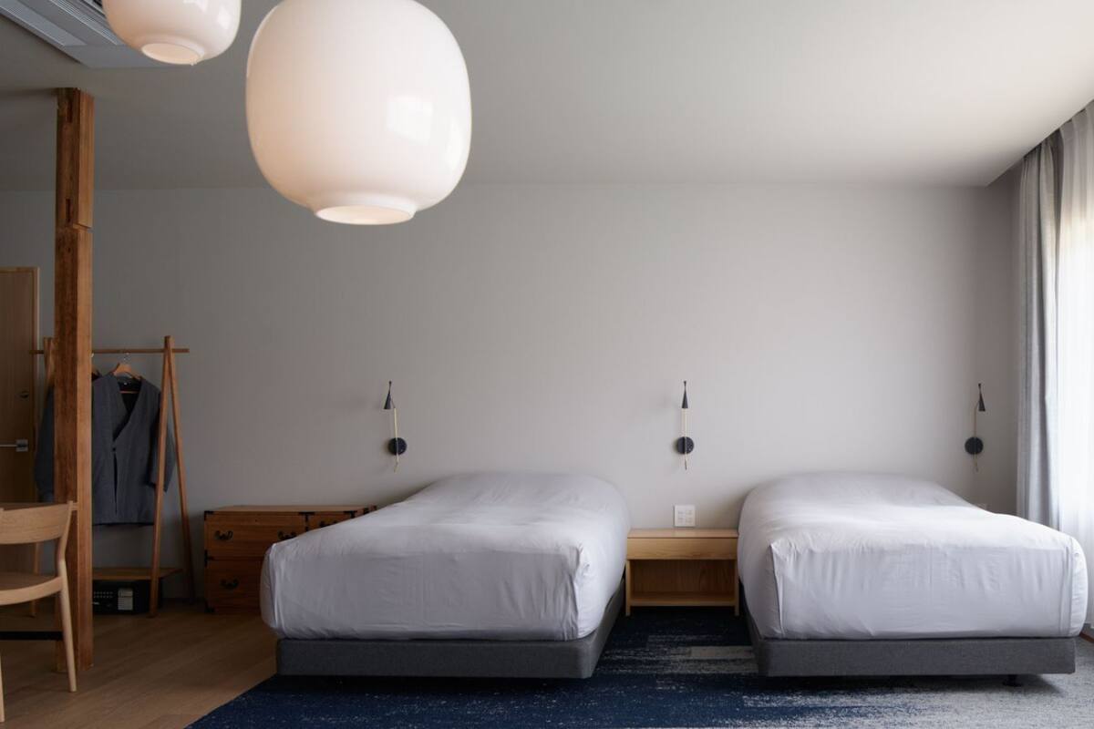 Una habitación de hotel moderna con dos camas individuales, un escritorio de madera, una silla y un perchero.
