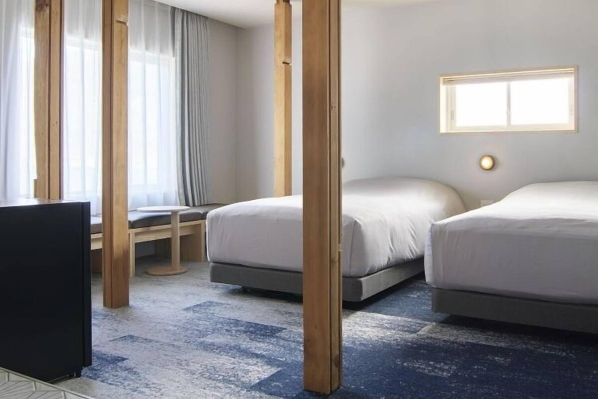 Habitación de hotel con dos camas, un escritorio, una silla y un televisor.