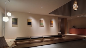 Un área de espera moderna con disposición de asientos en banca, iluminación colgante y obras de arte en las paredes.