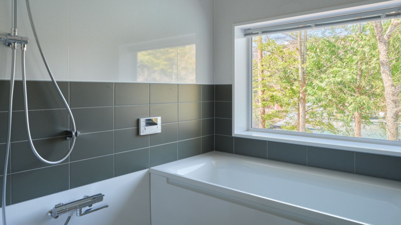 Een moderne badkamer met een bad, een douche en een raam met uitzicht op bomen.