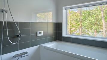 Een moderne badkamer met een bad, een douche en een raam met uitzicht op bomen.
