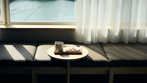 Asiento junto a la ventana con una mesita, una taza y un plato de comida.