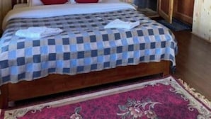 Una habitación con paneles de madera, una cama, una colcha a cuadros rojos y blancos, y un tapete floral rojo.