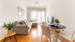 Een moderne woonkamer met een bank, een eettafel met stoelen, een televisie en een plant.