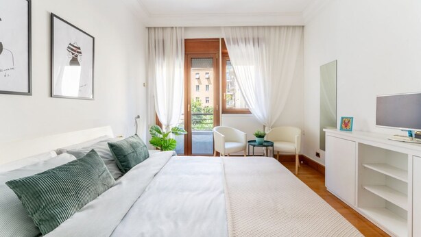 Een moderne slaapkamer met een bed, een bureau, een stoel, een televisie en een raam met gordijnen.