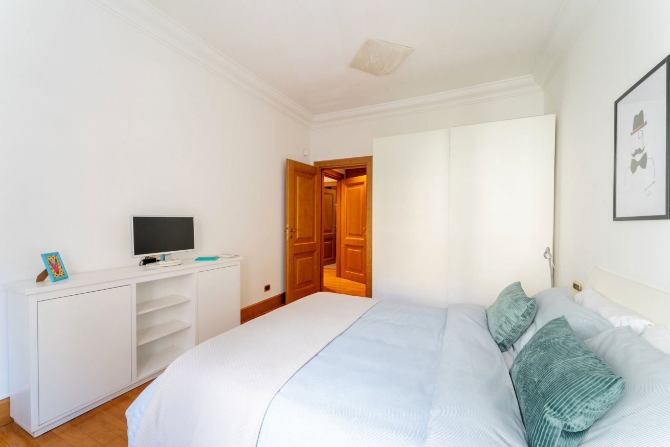 Una camera da letto con un letto, una TV su un mobile bianco e una porta che dà su un'altra stanza.
