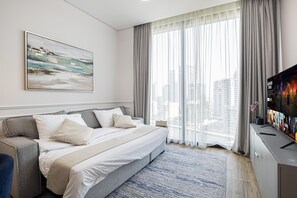 A modern hotel room with a large bed, a sofa, a TV, and a city view. - Modern Coastal Luxe  JBR Apartment (Dubai)