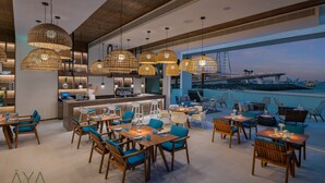 Un restaurante moderno con terraza y vistas a la ciudad, con lámparas colgantes de mimbre, mobiliario de madera y una zona de bar.