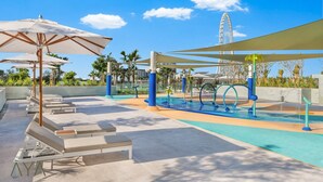 Un área de piscina en la azotea con sillones de descanso, sombrillas y una zona de juegos acuáticos.
