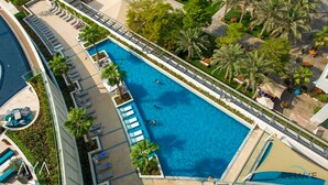 Vista aérea de un hotel con una piscina rectangular grande rodeada de palmeras y sillas de descanso.