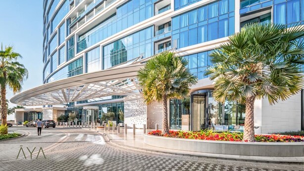 Un hotel moderno con una entrada curva, palmeras y fachada de vidrio.