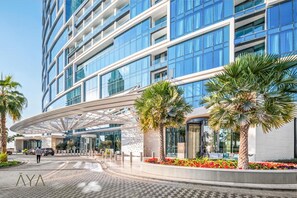 A modern hotel with a curved entrance, palm trees, and a glass facade. - Modern Coastal Luxe  JBR Apartment (Dubai)