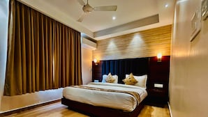 A modern bedroom with a large bed, wooden flooring, a ceiling fan, and a wall-mounted air conditioning unit. - Grand Pinnacle Lucknow (Lucknow)