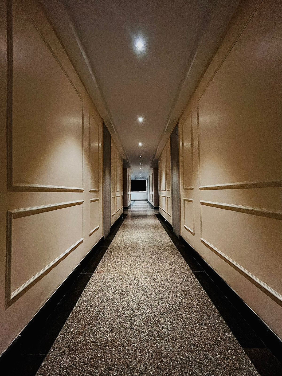A long, narrow hallway with cream-colored walls and a speckled carpet.