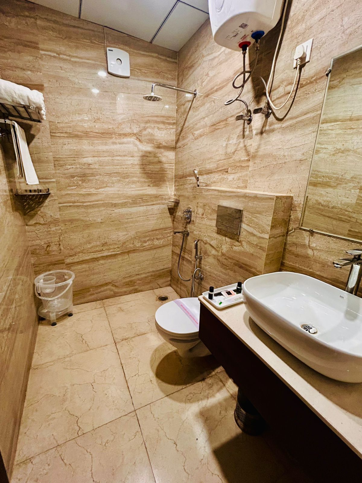 A bathroom with a marble floor, a white toilet, a large sink, and a shower with a handheld showerhead.