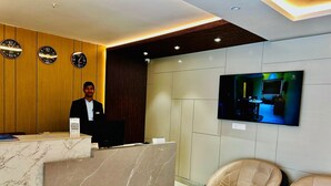 A hotel reception area with a marble reception desk, a receptionist, a mounted television, and two leather armchairs. - Grand Pinnacle Lucknow (Lucknow)