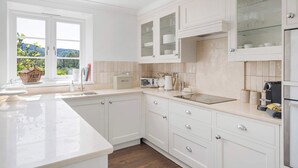 Une cuisine moderne avec des meubles blancs, une grande fenêtre et une vue sur la verdure.