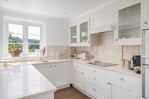 Une cuisine moderne avec des meubles blancs, une grande fenêtre et une vue sur la verdure.