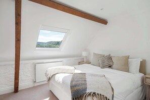 Una camera da letto con un lucernario, un letto con coperta a righe, una lampada da comodino e vista sul verde circostante.