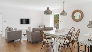 Una sala de estar moderna con un televisor de pantalla plana, sofás grises, sillas de madera e iluminación colgante.