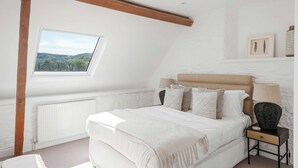 Une chambre avec un plafond en pente, un puits de lumière, un lit avec de nombreux oreillers, une table de chevet avec une lampe et un radiateur.