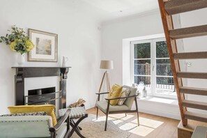 Un salon avec une cheminée, un fauteuil, une table et une fenêtre donnant sur un beau paysage.