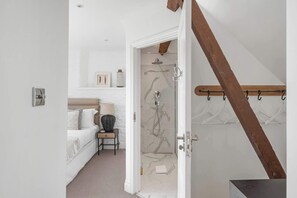 Un dormitorio con cama, mesita de noche, lámpara y vistas a un baño con ducha y toallero.