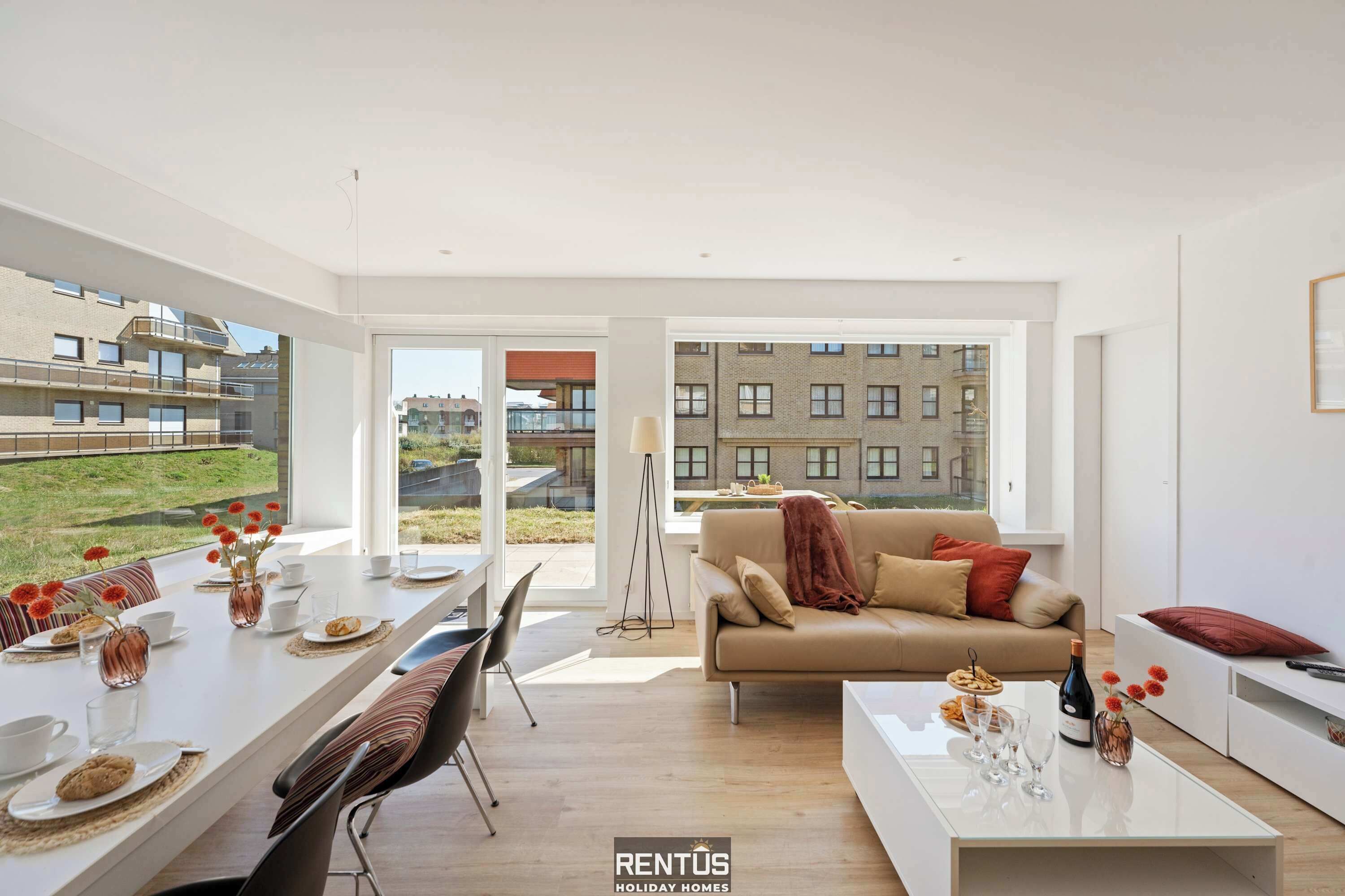 Ein modernes Wohnzimmer mit Essbereich, großen Fenstern und Blick auf Gebäude.
