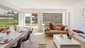 A modern living room with a dining area, large windows, and a view of buildings. - James Ensor Zon - beach fun in Oostduinkerke (Oostduinkerke)