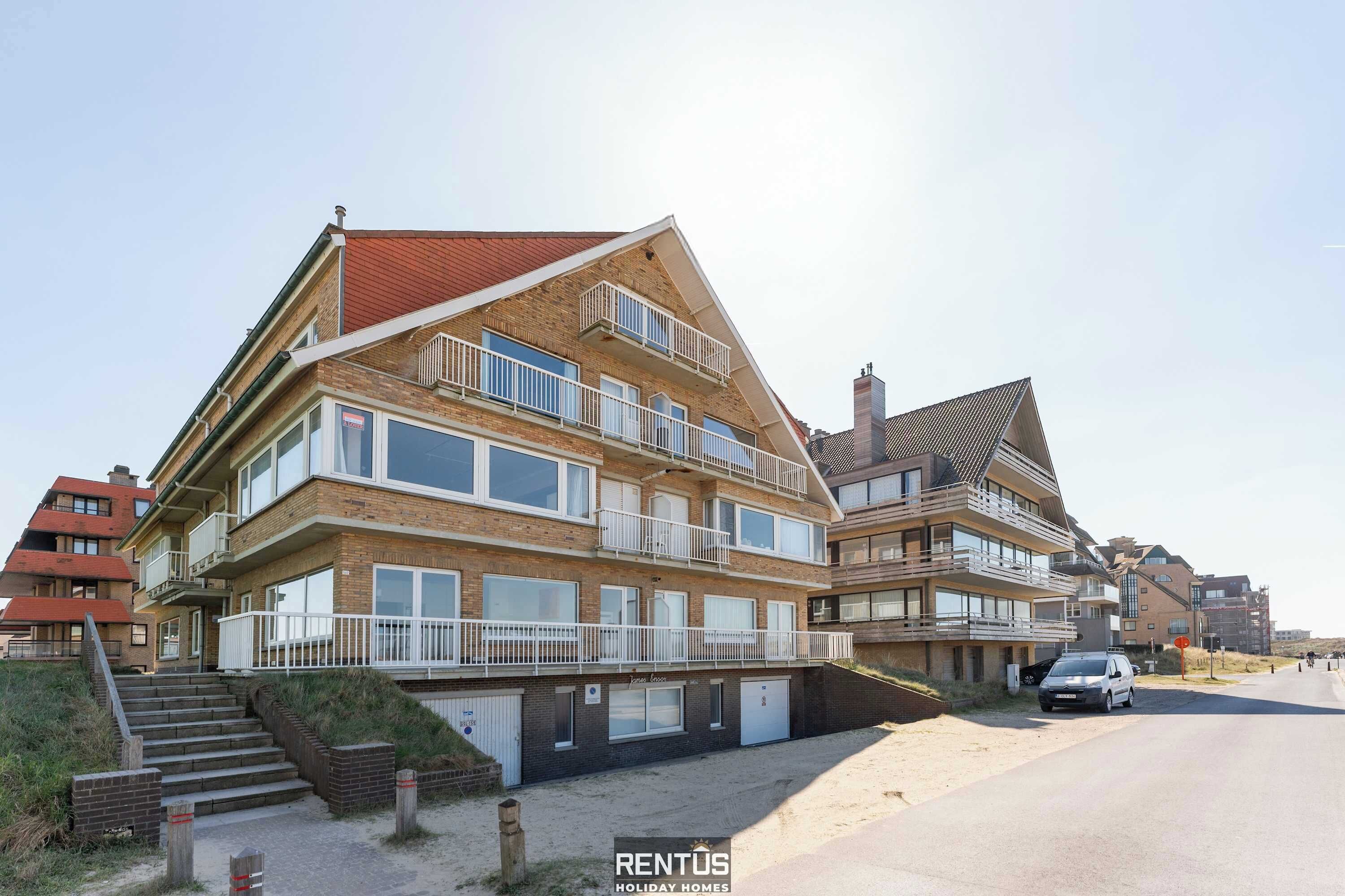A multi-story residential building with balconies, a garage, and a sandy driveway.