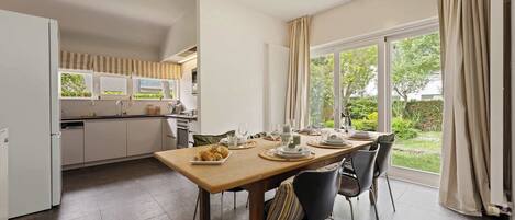 A modern kitchen with a dining area, large windows, and a view of the garden.