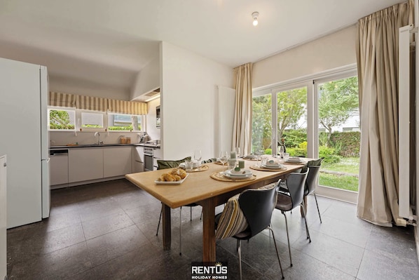 A modern kitchen with a dining area, large windows, and a view of the garden.