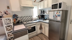 A compact kitchen with white cabinets, a stainless steel refrigerator, a microwave, a gas stove, and a small sink. - Mh 229 - La Tremblade: Comfortable Mobile Home for Families, Near Beach & City Center (La Tremblade)