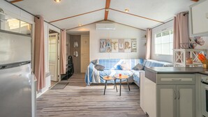 A compact kitchen with a refrigerator, a dining table with chairs, and a sofa in the living area. - Mh 229 - La Tremblade: Comfortable Mobile Home for Families, Near Beach & City Center (La Tremblade)
