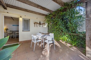 Une terrasse avec une table et des chaises, un plafond avec des poutres en bois et un mur recouvert de verdure.