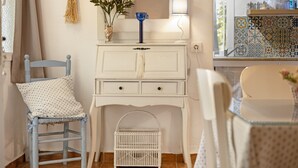 Una habitación con tocador blanco, una silla con cojín de lunares, jaula de pájaros blanca y salpicadero de azulejos.