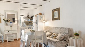 Una habitación con una mesa de comedor, sillas, un sofá, una mesita de noche con una lámpara y un cuadro colgado en la pared.