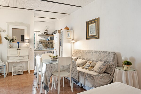 A room with a dining table, chairs, a sofa, a small table with a lamp, and a wall-mounted picture frame.