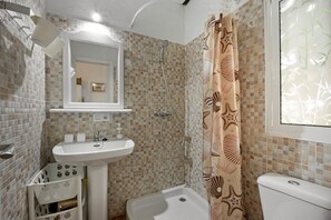 A bathroom with a tiled wall, a sink, a toilet, and a shower.