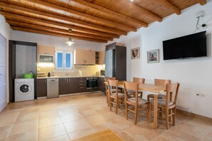 Une cuisine avec des meubles en bois, un lave-linge, une table à manger avec des chaises et un téléviseur à écran plat fixé au mur.