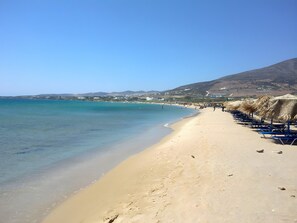 Una spiaggia con acque limpide, una battigia sabbiosa e una fila di ombrelloni di paglia.