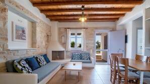 A cozy living area with a stone wall, wooden ceiling, a sofa, a table, and a dining set. - Holiday Home 'Blue Xenia' with Sea View, Wi-Fi and Air Conditioning (Chrisi Akti)