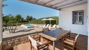 A covered outdoor area with a pool, lounge chairs, and a dining table. - Holiday Home 'Blue Xenia' with Sea View, Wi-Fi and Air Conditioning (Chrisi Akti)