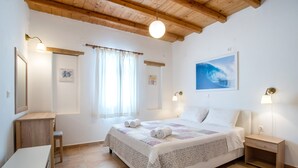 A bedroom with a bed, bedside tables, a desk, a chair, a window with curtains, and a painting on the wall. - Holiday Home 'Blue Xenia' with Sea View, Wi-Fi and Air Conditioning (Chrisi Akti)