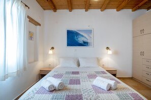 A bedroom with a bed, two bedside lamps, a painting, a wooden wardrobe, and a window with curtains.