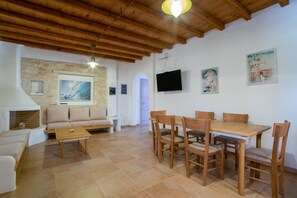 Et værelse med træloft, sofa, spisebord med stole, tv ophængt på væggen og kunstværker.