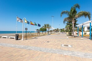 A paved walkway with flags, palm trees, and a beach in the background. - Apartment 'La Casita De La Playa' with Private Terrace, Wi-Fi and Air Conditioning (La Cala del Moral)